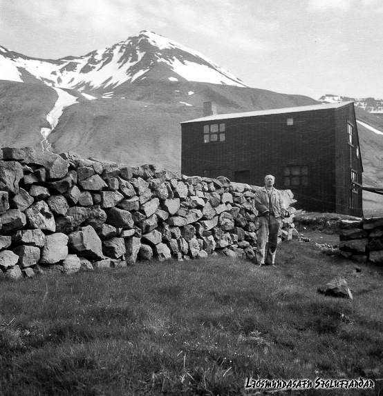 Aage Nörgaard. Ljósmyndari: Kristfinnur Guðjónsson
"Þetta er Aage Nörgaard, verkamaður við virki sitt Norðurgarður á Siglufirði, hús hans í bakgrunni.

Hús sem hann kveikti í þegar hann flutti heim til Danmerkur, en bænum var boðið að kaupa eignina, sem var afþakkað.